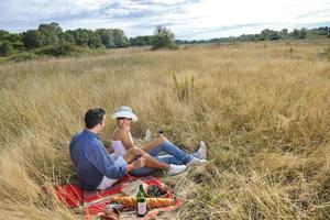 glückliches Paar, das ein Picknick auf dem Land im langen Gras genießt foto