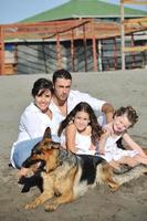 glückliche familie, die mit hund am strand spielt foto