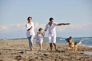 glückliche familie, die mit hund am strand spielt foto