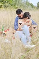glückliches Paar, das ein Picknick auf dem Land im langen Gras genießt foto
