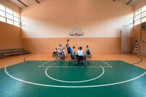 Behinderte Kriegsveteranen gemischte Rassen- und Alters-Basketballteams in Rollstühlen, die ein Trainingsspiel in einer Sporthalle spielen. Rehabilitations- und Inklusionskonzept für behinderte Menschen foto