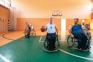 Behinderte Kriegsveteranen gemischte Rassen- und Alters-Basketballteams in Rollstühlen, die ein Trainingsspiel in einer Sporthalle spielen. Rehabilitations- und Inklusionskonzept für behinderte Menschen foto