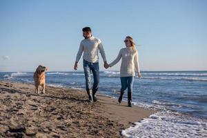 Paar mit Hund, das sich am Herbsttag am Strand amüsiert foto