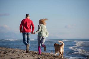 Paar mit Hund, das sich am Herbsttag am Strand amüsiert foto