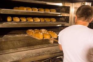 Bäckereiarbeiter, der frisch gebackenes Brot herausnimmt foto