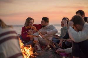 Gruppe junger Freunde, die am Feuer am Strand sitzen foto