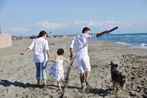 glückliche familie, die mit hund am strand spielt foto