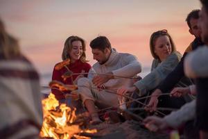 Gruppe junger Freunde, die am Feuer am Strand sitzen foto