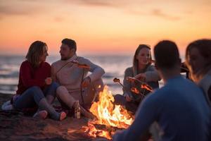 Gruppe junger Freunde, die am Feuer am Strand sitzen foto