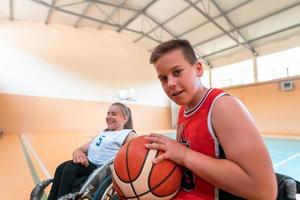 der junge sitzt im rollstuhl und bereitet sich auf den basketballstart des spiels in der großen arena vor. selektiver Fokus foto