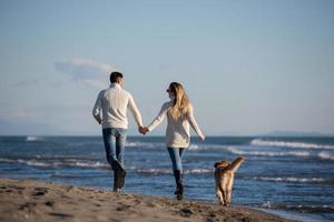 Paar mit Hund, das sich am Herbsttag am Strand amüsiert foto