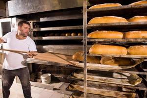 Bäckereiarbeiter, der frisch gebackenes Brot herausnimmt foto