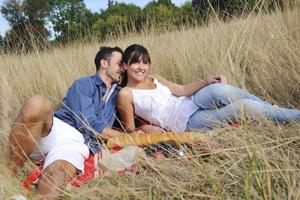 glückliches Paar, das ein Picknick auf dem Land im langen Gras genießt foto