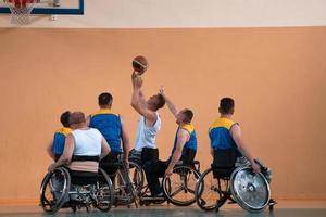 Behinderte Kriegsveteranen gemischte Rassen- und Alters-Basketballteams in Rollstühlen, die ein Trainingsspiel in einer Sporthalle spielen. Rehabilitations- und Inklusionskonzept für behinderte Menschen