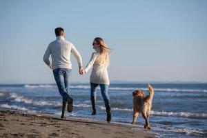 Paar mit Hund, das sich am Herbsttag am Strand amüsiert foto