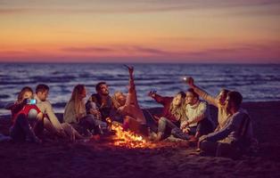 eine gruppe von freunden, die lagerfeuer am strand genießen foto