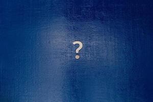 ein kleines Fragezeichen aus weißem Metall in der Mitte eines dunkelblau lackierten Bretts - flaches Lay-Konzept foto