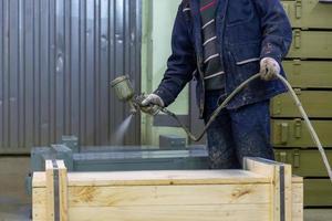 Arbeiter mit Airbrush malt große Holzkisten in grauer Farbe foto