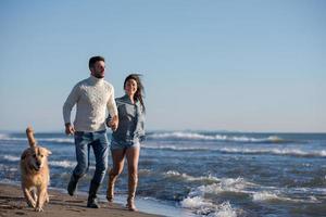 Paar mit Hund, das sich am Herbsttag am Strand amüsiert foto