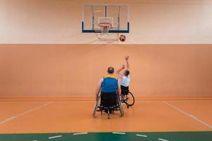 Behinderte Kriegsveteranen gemischte Rassen- und Alters-Basketballteams in Rollstühlen, die ein Trainingsspiel in einer Sporthalle spielen. Rehabilitations- und Inklusionskonzept für behinderte Menschen foto