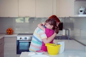 Der lustige Helfer des kleinen Mädchens, der mit Teig auf seinen Händen spielt und das Kneten lernt, hilft der erwachsenen Mutter in der Küche, der glücklichen süßen kleinen Tochter und der Elternmutter, viel Spaß beim Kochen von Keksen zu haben. foto