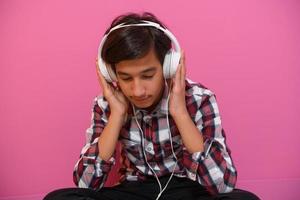 Arabischer Teenager, der Kopfhörer trägt und Musik auf rosafarbenem Hintergrund hört foto