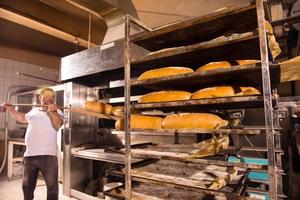 Bäckereiarbeiter, der frisch gebackenes Brot herausnimmt foto