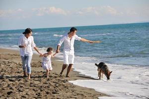 glückliche familie, die mit hund am strand spielt foto