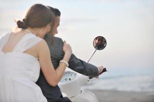 Gerade verheiratetes Paar am Strand fährt weißen Roller foto