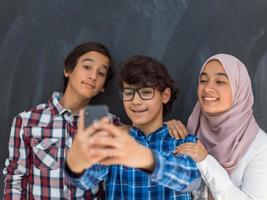 Gruppe arabischer Teenager, die Selfie-Foto auf Smartphone mit schwarzer Tafel im Hintergrund machen foto
