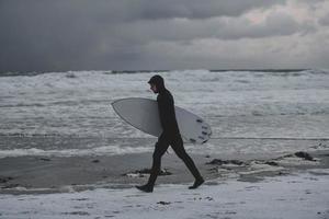 arktischer surfer, der nach dem surfen am strand vorbeigeht foto