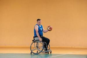 ein kriegsbeschädigter im rollstuhl trainiert mit einem ball in einem basketballverein beim training mit professionellen sportgeräten für behinderte. das Konzept des Sports für Menschen mit Behinderungen foto