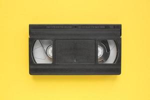 schwarze vhs-videorecorderkassette auf gelbem hintergrund. alte veraltete technologie für die bandaufzeichnung und das ansehen von medienfilmen. retro, vintage, geschichte, nostalgiekonzept. Ansicht von oben, flach liegend foto