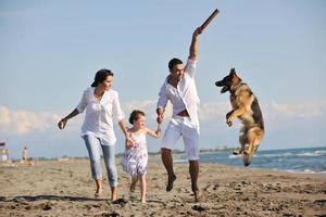 glückliche familie, die mit hund am strand spielt foto