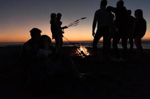 Paar genießt Lagerfeuer mit Freunden am Strand foto