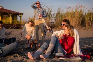 Paar genießt mit Freunden den Sonnenuntergang am Strand foto