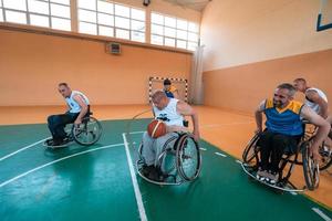 Behinderte Kriegsveteranen gemischte Rassen- und Alters-Basketballteams in Rollstühlen, die ein Trainingsspiel in einer Sporthalle spielen. Rehabilitations- und Inklusionskonzept für behinderte Menschen foto