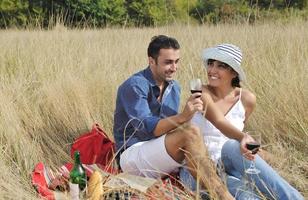 glückliches Paar, das ein Picknick auf dem Land im langen Gras genießt foto