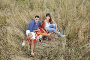 glückliches Paar, das ein Picknick auf dem Land im langen Gras genießt foto