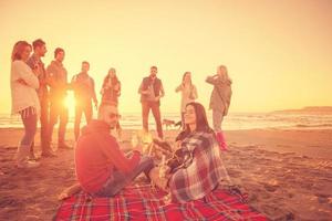 Paar genießt mit Freunden den Sonnenuntergang am Strand foto