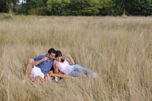 glückliches Paar, das ein Picknick auf dem Land im langen Gras genießt foto