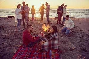 Paar genießt mit Freunden den Sonnenuntergang am Strand foto