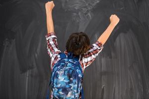 Junge feiert eine erfolgreiche Schulzeit mit erhobenen Händen, während er vor der Schultafel steht foto