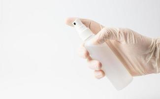 eine Hand in einem Schutzhandschuh, der einen Behälter mit einer antibakteriellen Flüssigkeit auf weißem Hintergrund hält. das Konzept der Aufrechterhaltung der Hygiene während einer Pandemie. foto
