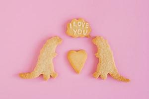 hausgemachte Shortbread-Kekse mit weißer Glasur auf rosa Hintergrund, Draufsicht. zwei dinosaurier mit legende wolke mit text - ich liebe dich foto