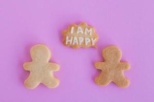 hausgemachte Shortbread-Kekse mit weißer Glasur auf rosa Hintergrund, Draufsicht. Zwei Personen mit Legende Wolke mit Text - ich bin glücklich foto