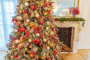 klassischer weihnachtlich dekorierter innenraum, neujahrsbaum mit roten und goldenen dekorationen. Modernes, weißes Innendesign-Apartment im klassischen Stil mit Kamin und Weihnachtsbaum. Heiligabend zu Hause. foto