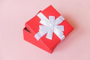 weihnachten neujahr geburtstag valentinstag feier vorhanden romantisches konzept. einfach minimalistisches Design rote Geschenkbox isoliert auf pastellrosa farbigem Hintergrund. Flache Ansicht von oben, Kopierbereich foto