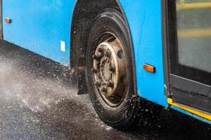 blauer stadtbus, der auf regnerischer straße mit wasserspritzern fährt foto