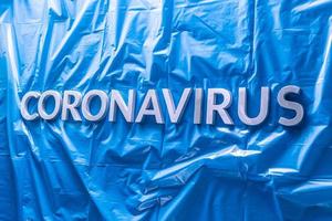 Wort Coronavirus mit silbernen Buchstaben auf zerknittertem blauem Plastikmantel - in perspektivischer Ansicht mit selektivem Fokus foto